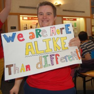A person holding up a sign that says " we are here alike than different ".