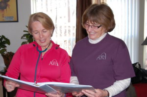 Two women standing next to each other holding papers.
