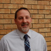 A man in a blue tie standing next to a brick wall.
