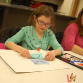 A girl is sitting at the table and making something.