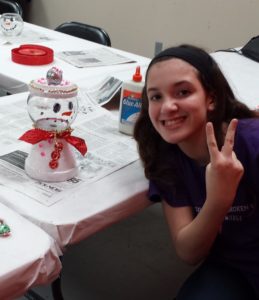 A girl sitting at the table with her hand up to sign.