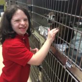 Neighborhood Experiences participant with brown hair and red shirt smiling as she pets a brown dog through a cage