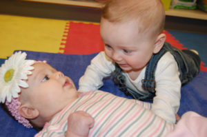 A baby and an infant playing together on the floor.