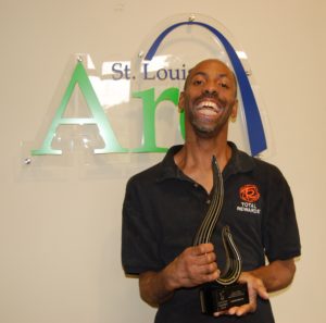 A man holding a trophy in front of a st louis arch.