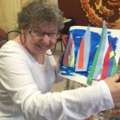 A woman holding up a paper boat with colorful sails.