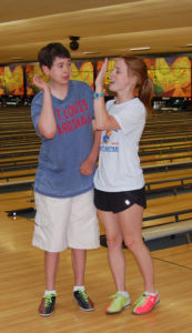 A boy and girl standing in front of bowling lanes.
