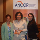 Three women are posing for a picture with an ancor banner behind them.