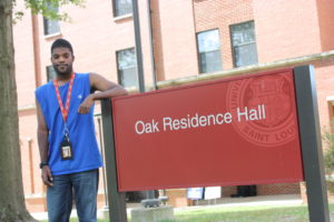 A man standing next to an oak residence hall sign.