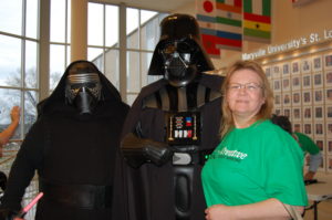 A woman standing next to two people dressed as darth vader and princess leia.
