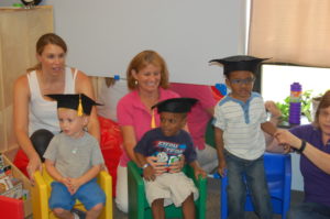A group of children sitting in chairs wearing graduation hats.
