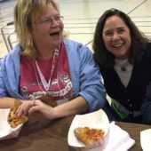 Two women sitting at a table with some pizza.