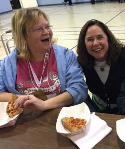 Two women sitting at a table with some pizza.