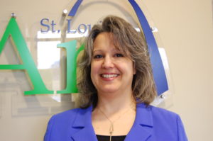 A woman in blue jacket standing next to a wall.