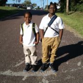 Two boys standing on the side of a road.