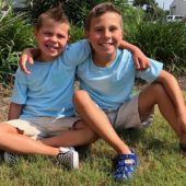 Two boys sitting on the grass in front of some bushes