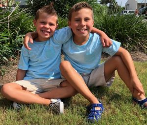 Two boys sitting on the grass in front of some bushes