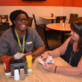 Two women sitting at a table with drinks and food.