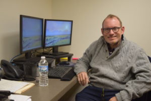 A man sitting at his computer desk with two monitors.