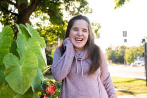 A girl in purple hoodie laughing while standing next to a tree.