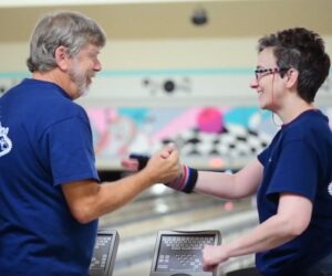 Two people shaking hands in a bowling alley.