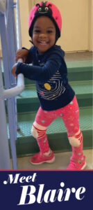 A young child wearing a helmet and holding onto the handle of a stair rail.