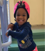 A young child wearing a helmet and holding onto the handle of a stair rail.