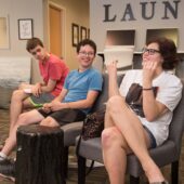 Three people sitting in a room with remotes.