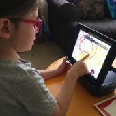 child with red glasses using an ipad to draw circles