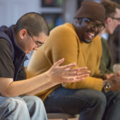 Two young men laugh while talking in a group setting