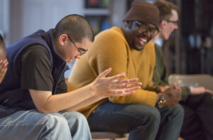 Two young men laugh while talking in a group setting