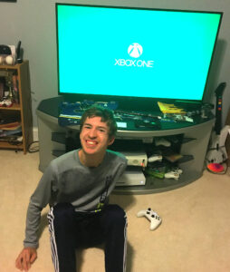 Young man sitting on the floor in front of a TV with the XBox logo.