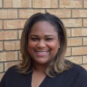 Smiling woman in front of brick building wearing black v neck shirt