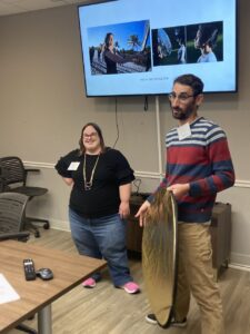 A professor holds a reflector board as a student stands next to him listening.