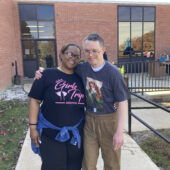 A staff member and a resident pose for a photo outside of the residential buildings