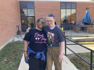 A staff member and a resident pose for a photo outside of the residential buildings