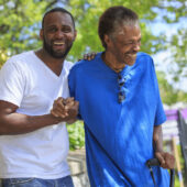 A younger man supports an older man with his hand and arm.