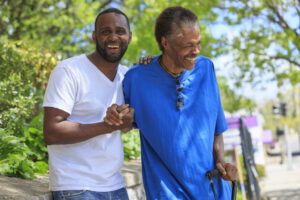 A younger man supports an older man with his hand and arm.