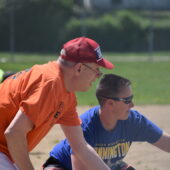 A coach points in the field, showing a softball player what to do.