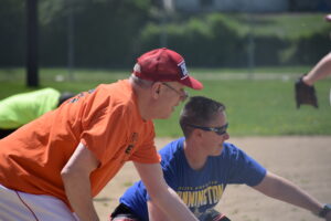 Two men are sitting on the ground in a baseball field.