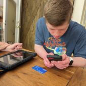 A boy is looking at his phone while sitting on the table.